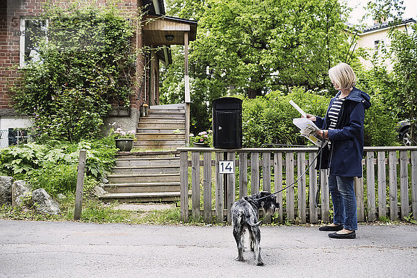 Seniorin prüft Briefe im Stehen mit Hund vor dem Haus