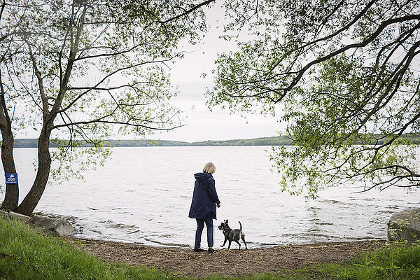 Rückansicht einer älteren Frau mit Hund am Seeufer
