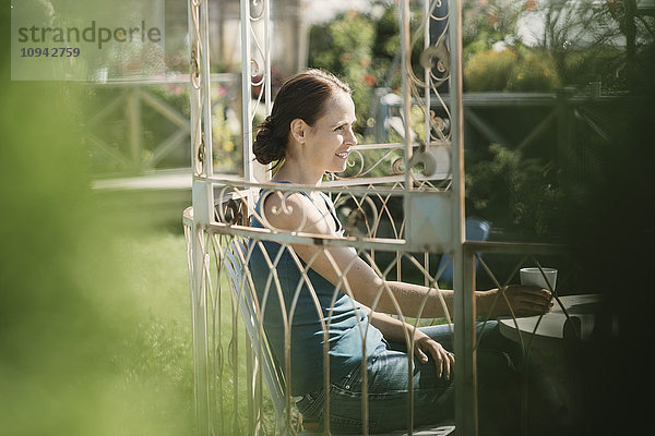Fröhliche erwachsene Frau mit Kaffeetasse im Hinterhof