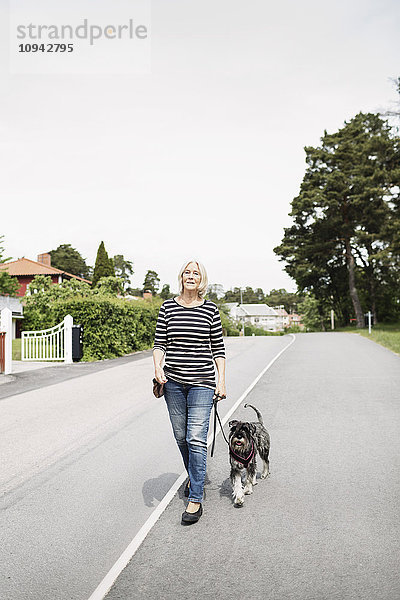 Volle Länge der älteren Frau  die mit Hund auf der Straße spazieren geht