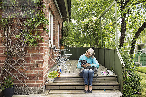 Glückliche Frau sitzend mit Hund auf Stufen vor dem Haus