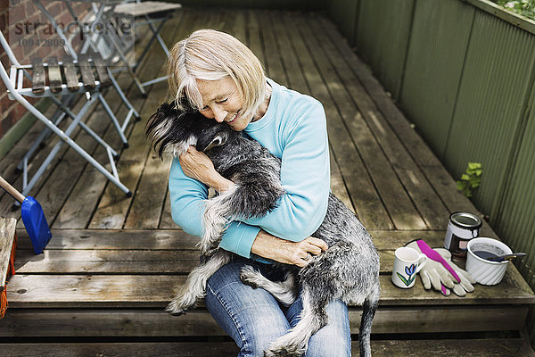 Fröhliche Seniorin umarmt den Hund auf der Veranda