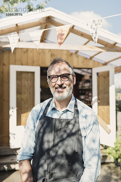 Portrait eines glücklichen reifen Ladenbesitzers  der sich gegen den Laden stellt.