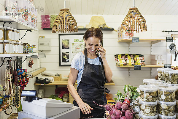 Fröhliche Frau beim Telefonieren am Ladentisch im Geschäft