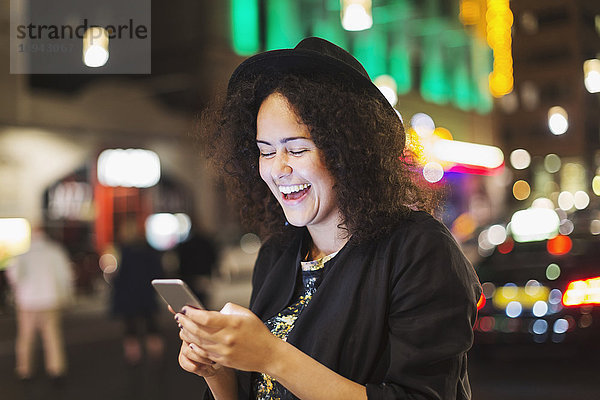Junge Frau lacht  während sie nachts in der Stadt Smartphones benutzt.