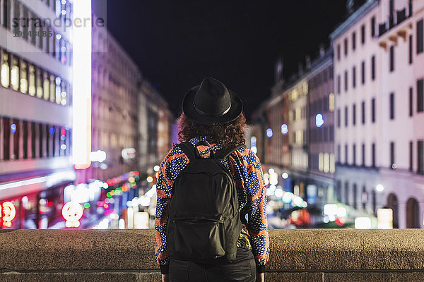 Rückansicht der Frau mit Rucksack auf der Brücke in der Stadt bei Nacht