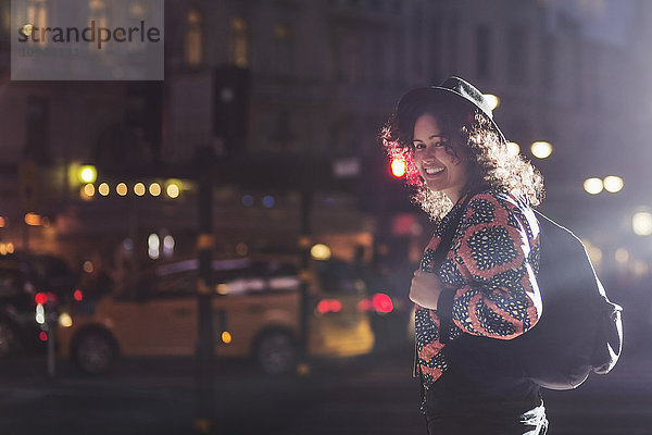 Seitenansicht Porträt einer lächelnden Frau  die nachts auf der Straße steht.