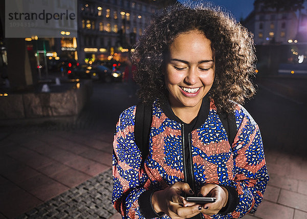 Glückliche junge Frau mit Smartphone in der Stadt bei Nacht