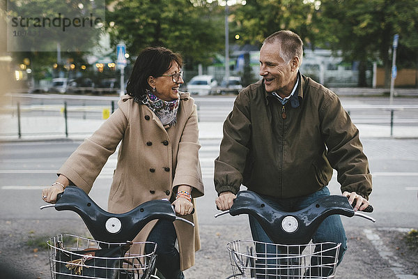 Glückliches Seniorenpaar mit Leihfahrrädern auf dem Parkplatz