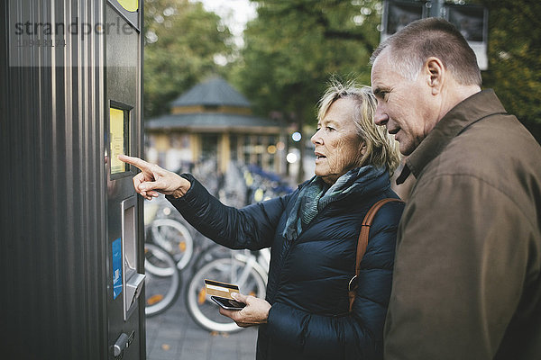 Senior Mann mit Frau bei der Bezahlung per Kreditkarte an der Fahrradverleihstation