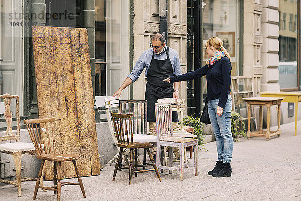 Die Kundin zeigt auf den Stuhl vor dem Antiquitätengeschäft.