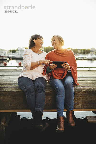 Volle Länge der glücklichen Seniorinnen mit digitalem Tablett am Pier