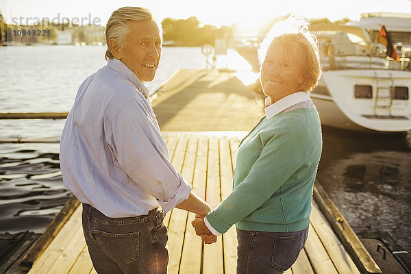 Porträt eines glücklichen älteren Paares  das am Pier Händchen hält.