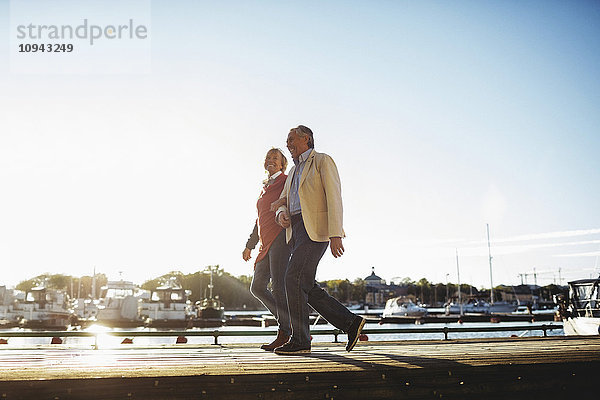 Volle Länge des liebenden älteren Paares  das auf dem Pier gegen den Himmel geht.