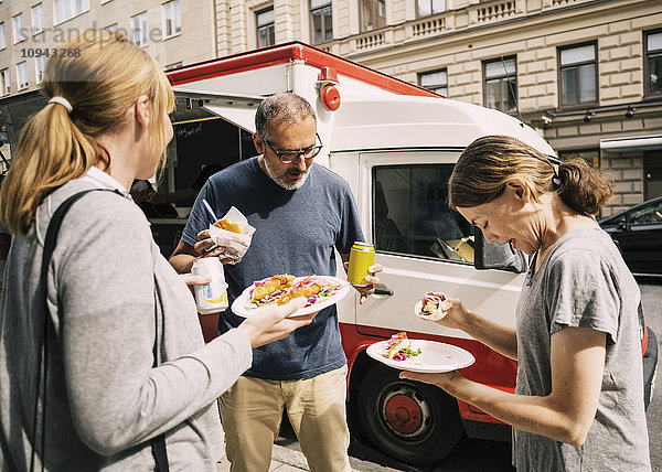 Leute  die Essen essen  während sie auf der Straße stehen.