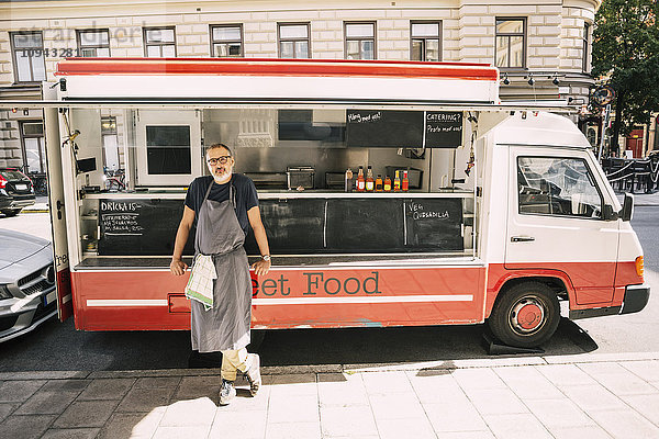 Volle Länge des männlichen Kochs  der an der Stadtstraße gegen den Speisewagen steht.