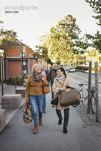 Männliche und weibliche Senioren  die mit Gepäck auf dem Bürgersteig spazieren gehen.