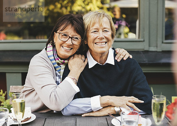 Lächelnde Senioren-Freundinnen mit Arm am Kaffeetisch
