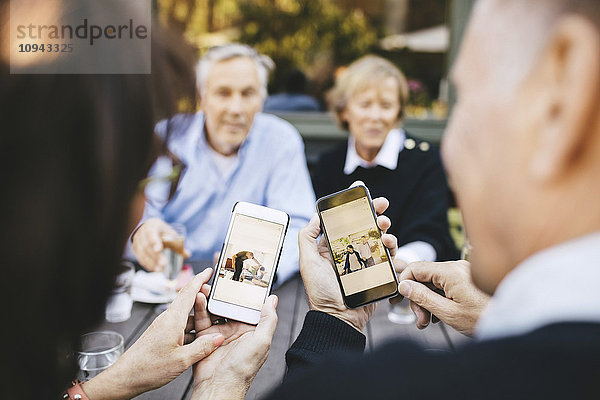 Seniorenpaar beim Betrachten von Fotos auf dem Handy im Außenrestaurant