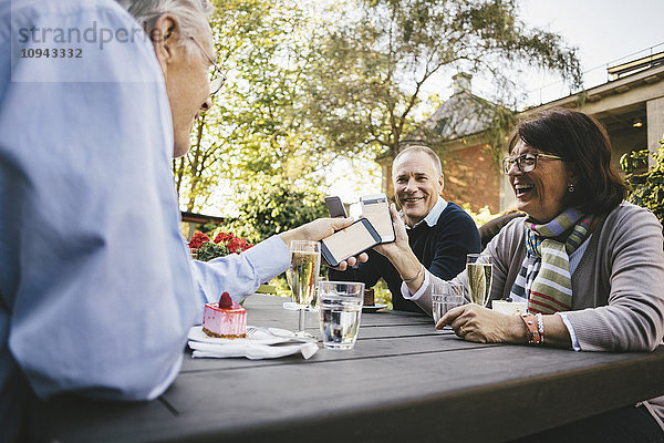 Glückliche Seniorenfreunde mit Mobiltelefonen im Outdoor-Café