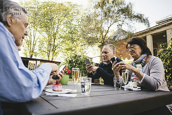 Senioren  die Mobiltelefone am Tisch des Außenrestaurants benutzen