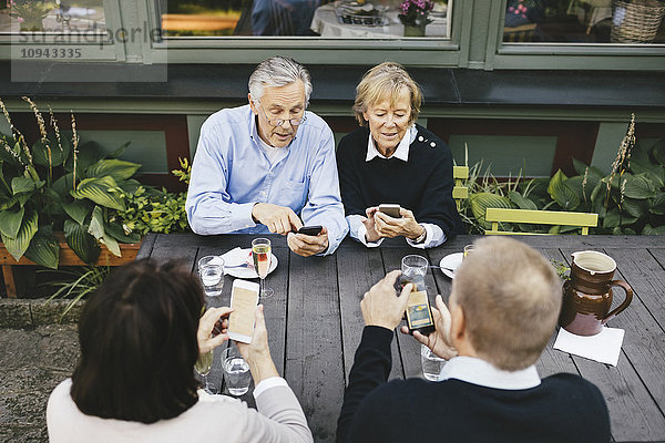 Zwei ältere Paare  die Mobiltelefone am Tisch des Außenrestaurants benutzen.