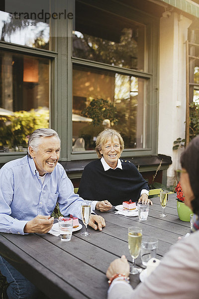 Lächelnder älterer Mann mit weiblichen Freunden beim Dessert im Außenrestaurant