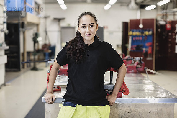 Porträt einer lächelnden Automechanikerin  die in der Werkstatt steht.