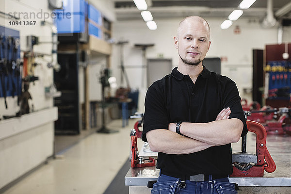 Porträt eines selbstbewussten Automechanikers mit gekreuzten Armen in der Werkstatt