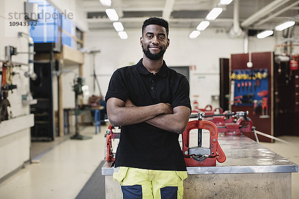 Porträt eines lächelnden Automechanikers mit gekreuzten Armen in der Werkstatt