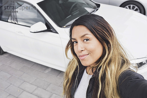 Hochwinkel-Porträt einer lächelnden jungen Frau  die gegen das Auto steht.