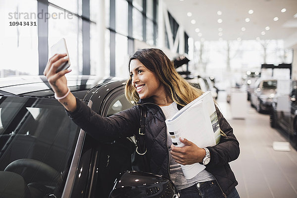 Lächelnde Frau nimmt Selfie mit neuem Auto in den Showroom