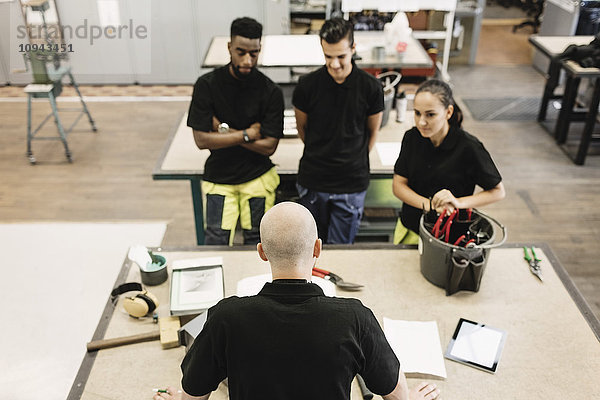 Gymnasiallehrer unterrichtet Schüler bei Tisch im Workshop