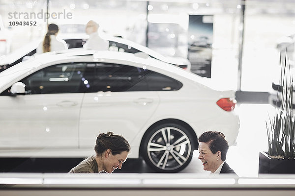 Lächelnde Frauen diskutieren mit dem Auto im Showroom