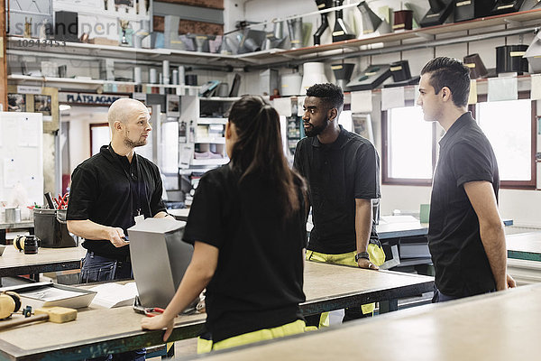 Gymnasiallehrer im Gespräch mit Schülern am Tisch im Workshop