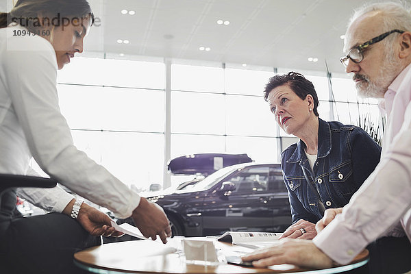 Verkäuferin  die den Kunden im Autohaus Dokumente erklärt