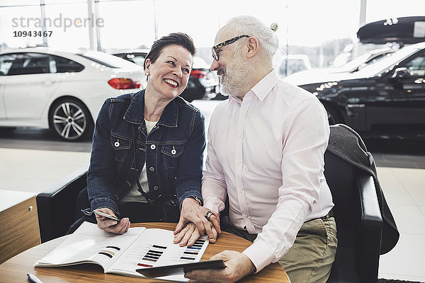 Fröhliches Seniorenpaar liest Broschüre im Autohaus