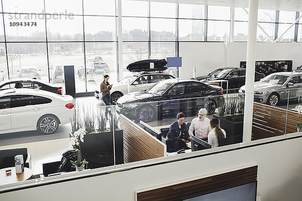 Autoverkäufer im Gespräch mit Kunden am Schreibtisch im Showroom