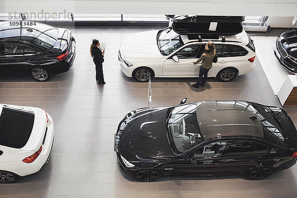 Hochwinkelansicht der Verkäuferin und des Kunden beim Betrachten des Autos im Showroom