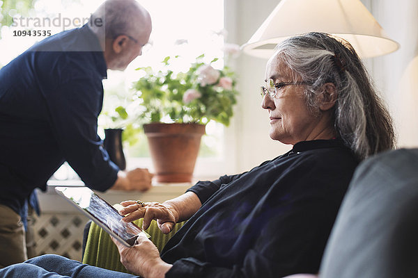 Seitenansicht der älteren Frau mit digitalem Tablett  während der Mann auf die Pflanze schaut