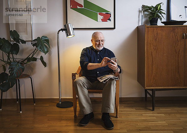 Senior Mann mit Handy auf dem Stuhl zu Hause