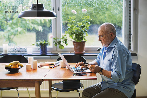 Seitenansicht des älteren Mannes mit Kreditkarte für den Online-Shopping zu Hause