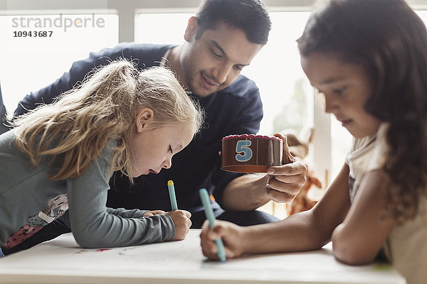 Mädchen zeichnen  während der Lehrer im Klassenzimmer einen Nummernblock hält.