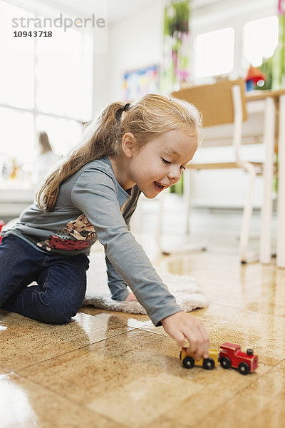 Glückliches Mädchen spielt mit Spielzeugauto auf dem Boden im Klassenzimmer