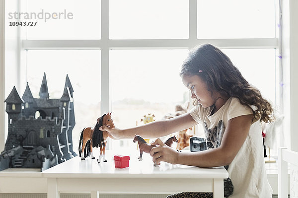 Seitenansicht des Mädchens beim Spielen mit Spielzeugpferden am Tisch