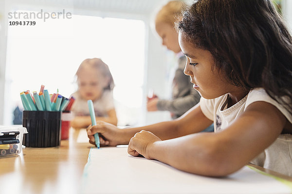 Mädchen mit Filzstift in der Zeichenklasse mit Klassenkameraden im Hintergrund