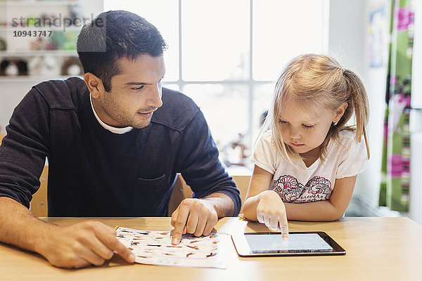 Mittlerer Erwachsener  männlicher Lehrer  der ein Mädchen mit einem digitalen Tablett im Vorschulalter betrachtet.