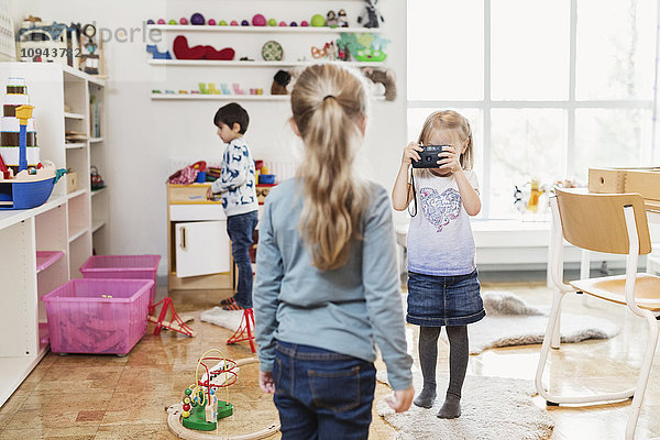 Kleines Mädchen beim Fotografieren des Freundes durch die Spielzeugkamera im Klassenzimmer