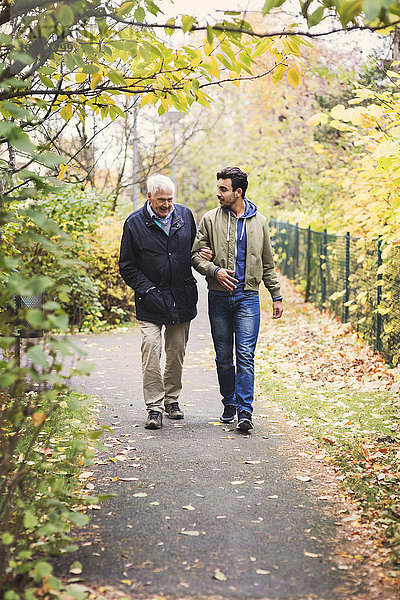 Volle Länge eines glücklichen älteren Mannes mit Hausmeister  der im Park spazieren geht.