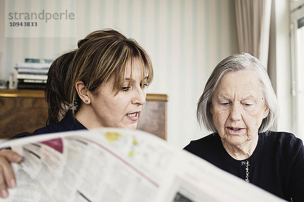 Hausmeisterin mit Seniorin beim Zeitungslesen im Pflegeheim